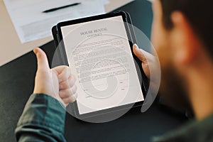 Close up male person reading house rental contract on tablet.