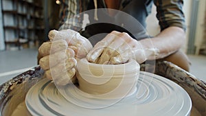 Close-up of male potter`s hands manufacturing ceramic bowl from clay using throwing wheel