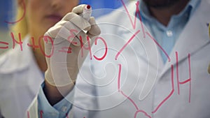 Close up of male researcher drawing chemical formula on glass