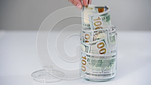 Close-up male's hand takes out a banknote from a jar full of hundred-dollar bills. The concept of spending money from