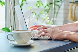 Close-up of male& x27;s hands typing on laptop keyboard, in coffee shop, with cup of coffee