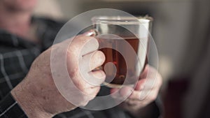 Close-up of male senior caucasian hands holding cup of tea. Unrecognisable pensioner waving to someone away. Lifestyle