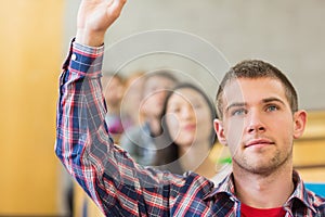 Close up of a male student raising hand by others in classroom