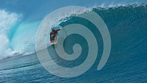 CLOSE UP: Male surfboarder drags his hand behind him while he surfs a tube wave.