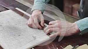 Close up of man with apron making a new brown leather belt in the leather workshop. Working process of the leather belt