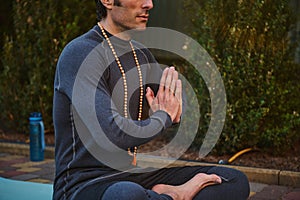 Close-up man athlete, yogi sitting folded palms together, practicing yoga outdoors. Prayer, gratitude. Spiritual growth