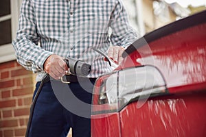 Close Up Of Man Attaching Charging Cable To Environmentally Friendly Zero Emission Electric Car At Home