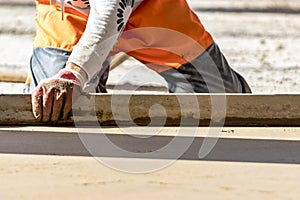 Close up of man builder placing screed rail on the floor covered with sand-cement mix at construction site. Male worker leveling