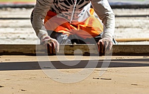 Close up of man builder placing screed rail on the floor covered with sand-cement mix at construction site. Male worker leveling