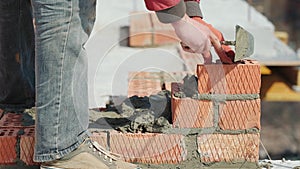 Close up of a man building a brick house. Laying red bricks on a construction site on a sunny day. House construction