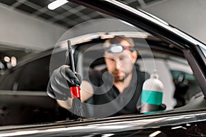 Close up of man, car service station worker, making cleaning and care procedures for car door interior, using brush and