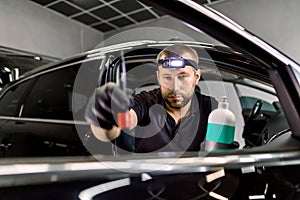 Close up of man, car service station worker, making cleaning and care procedures for car door interior, using brush and
