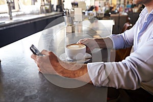 Close Up Of Man Checking Messages On Phone In Coffee Shop photo