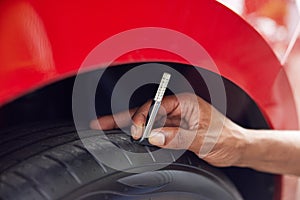 Close-Up Of Man Checking Tread On Car Tyre With Gauge