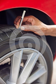 Close-Up Of Man Checking Tread On Car Tyre With Gauge