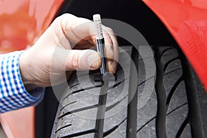 Close-Up Of Man Checking Tread On Car Tyre With Gauge