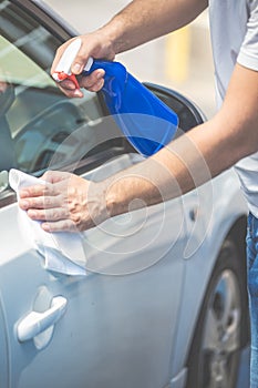 Close up of man cleaning car with cloth and spray bottle, car maintenance concept