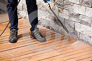 Close up of a man cleaning terrace with a power washer - high water pressure cleaner on wooden terrace surface