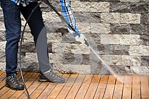 Close up of a man cleaning terrace with a power washer - high water pressure cleaner on wooden terrace surface