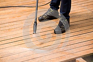 Close up of a man cleaning terrace with a power washer - high water pressure cleaner on wooden terrace surface