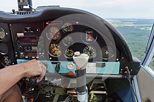 Close up of a man in a cockpit piloting small four seat airplane, pushing buttons on control panel with hills and meadows in