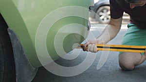 Close-up of a man connecting a tow rope to a non-working car at the side of the road.