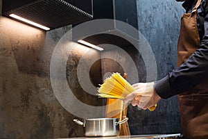 Close-up. A man cooks spaghetti in the kitchen. He dips the pasta into a pot of boiling water.