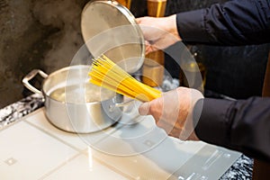 Close-up. A man cooks spaghetti in the kitchen. He dips the pasta into a pot of boiling water.