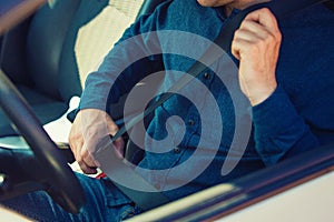 Close up man driver fastening seat belt. Guy seated behind the steering wheel testing his new car safety photo