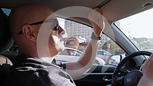 A close-up of a man driving a car, he lowers the sun visor.