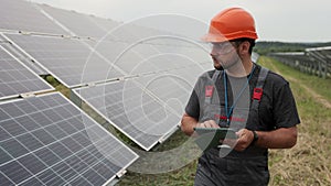 Close up of man engineer in working clothes walks on renewable energy station holding digital tablet and checking solar