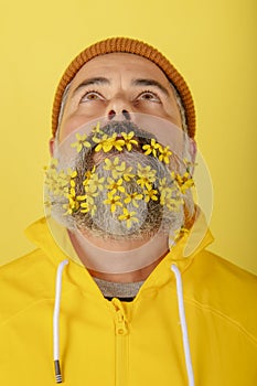 Close-up of man with flowers in his beard, standing against a yellow background looks up. Vertical picture