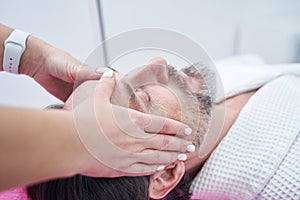 Close up of man getting facial massage and relaxing with eyes closed at spa