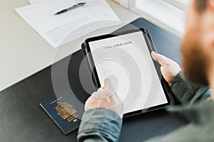 Close up man getting visa and reading application on tablet, passport on desk.