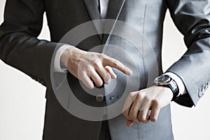 Close up of a man in grey suit pointing at watch on his hand wit