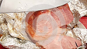 Close up of man hand with chrome long and sharp knife cutting roast pork ham in aluminum foil