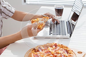 Close up man hand eating pizza while working in laptop computer