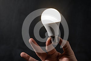 Close-up of man hand holding energy saving LED lamp. Saving energy and energy crisis concept. Lightbulb on the black background