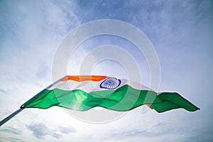 Close up man hand holding India flag on the blue sky background.