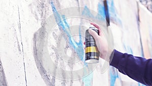 Close up of man hand holding spray paint against the concrete building wall. Action. Teenager holding a can of paint