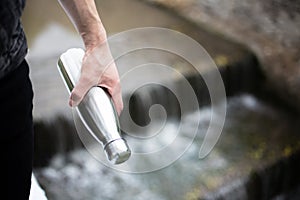 Close-up of man hand holding steel bottle for water, on river background.