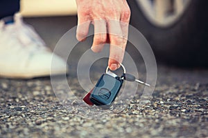 Close up of man hand lifting car keys fallen on the ground. Guy found vehicle keys someone lost on the asphalt road in the parking
