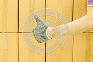 Close-up of man hand with thumb up in front of cardboard boxes, likes or approves concept