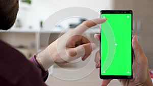 Close up of man hand touching and using a smartphone with green screen chroma mock up on it