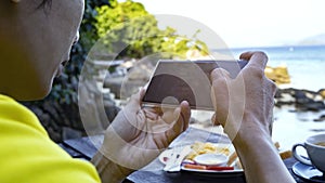Close up of Man hand using or looking at his smartphone and having lunch in the restaurant  near a sand beach beackground