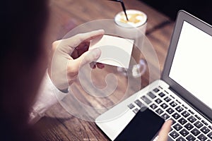 Close-up of man hands holding business card, working on laptop in cafe with internet, drinking latte