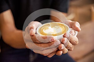 Close up man hands holding latte art coffee cup in cafe coffee shop. Hot coffee mug in man hands. Milk latte art fresh, relax in