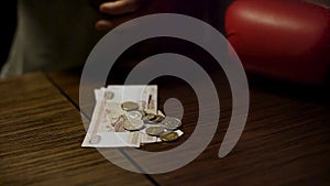 Close up of man hands holding an open leather wallet with a few coins inside over a old wooden table with paper money