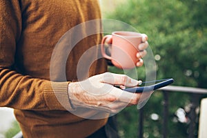 Close-up of man hands holding and using cell phone while drinking coffee.