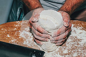 Close-up of man hands kneading bread dough on a cutting board
